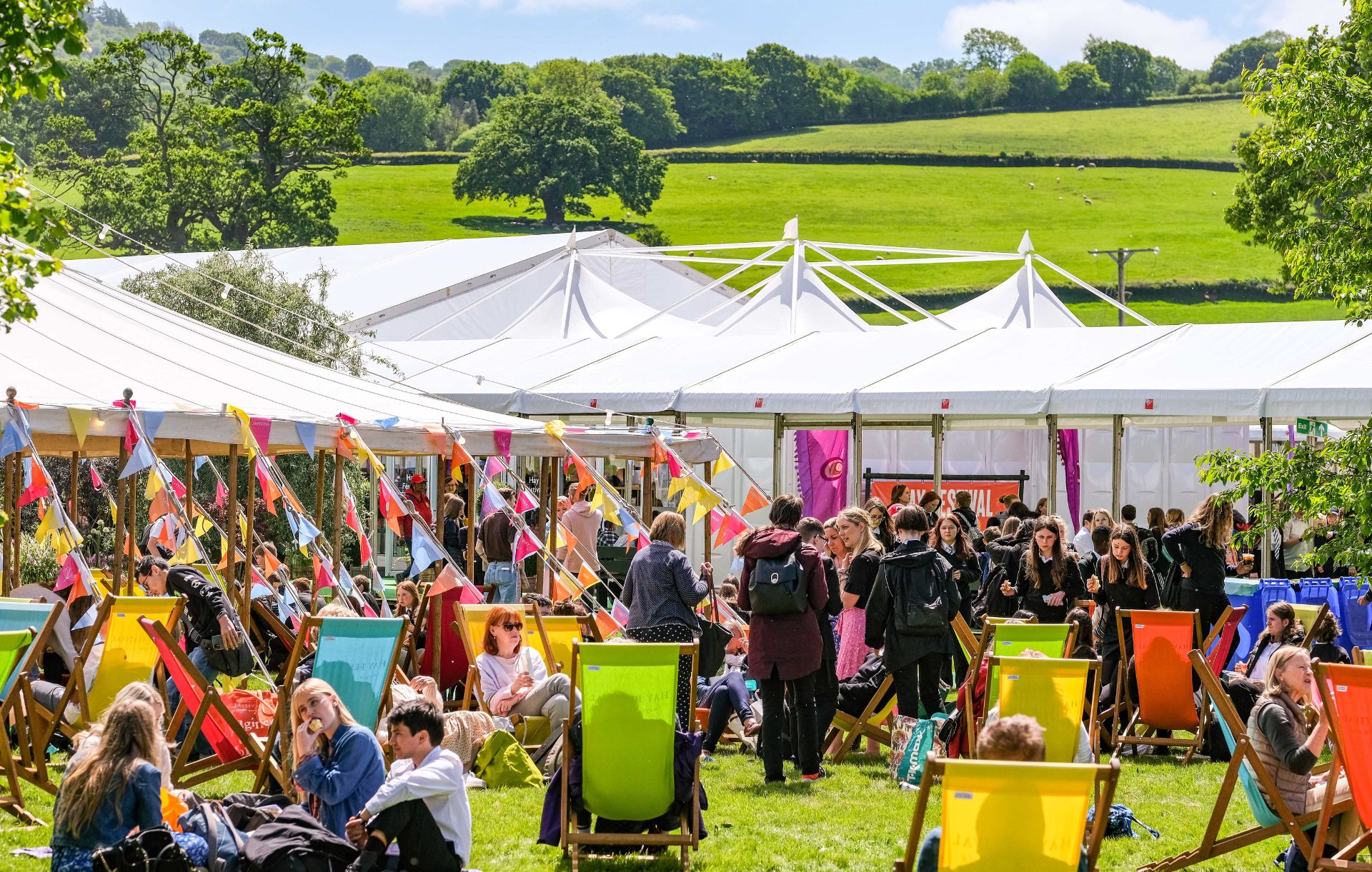 A festival scene, with marquees, bunting and people on deck chairs