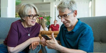A man and a woman sitting next to each and looking at a mobile phone the man is holding