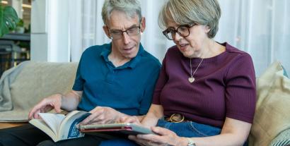 A man and a woman sitting next to each and looking at a tablet the woman is holding