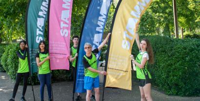 Three women and two men in running outfits holding large flags and looking at the camera