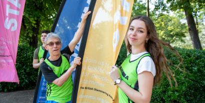 A man and a woman in running vests holding a flag and looking at the camera