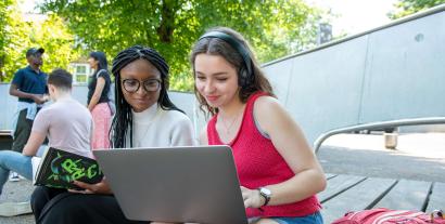 A woman in headphones showing something on her laptop to the woman sitting next to her.