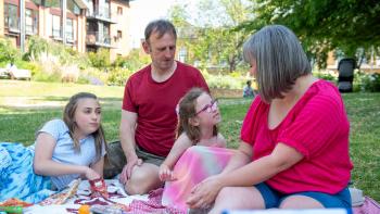 A family picnic, with a young girl speaking and her mother, father and daughter sitting listening to her