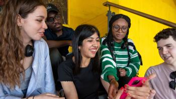 Three women and two men sitting together and looking at a mobile phone being held by one of the women