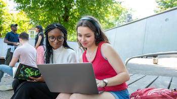 A woman in headphones showing something on her laptop to the woman sitting next to her.
