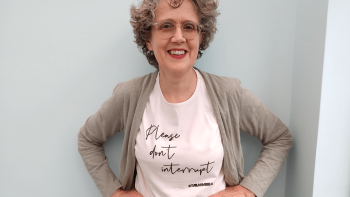 A woman with her hands on her hips, smiling for the camera. She is wearing a t-shirt that reads 'Please don't interrupt'.
