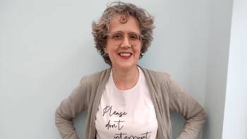 A woman with her hands on her hips, smiling for the camera. She is wearing a t-shirt that reads 'Please don't interrupt'.