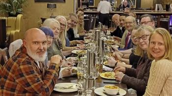 A group of people sitting around a restaurant table, looking at the camera and smiling