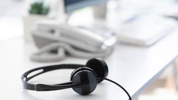 A pair of headphones on a desk, with a telephone behind it