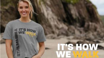 A woman standing on a beach looking at the camera. Next to her are the words 'Its how we walk'