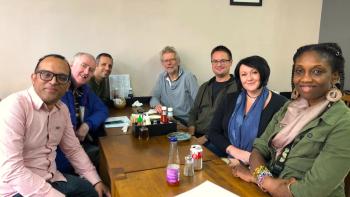 Seven people sitting around a cafe table smiling for the camera