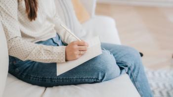A woman sitting on a sofa writing in a diary. Her face is not in view