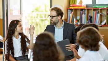 A teacher in a class speaking to a pupil, with the class sitting in a circle. The pupil, a girl, has her hand raised