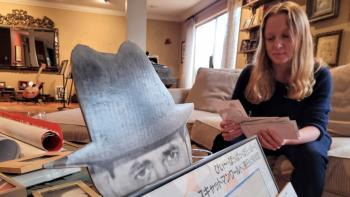 A woman sitting on a sofa, going through a set of photographs, with various items of memorabilia in front of her