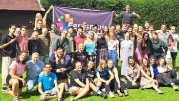 A big group of people, huddled together and smiling, some standing, some sitting and crouching