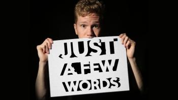 A man holding a sign up to cover his mouth. The sign reads 'Just a few words'