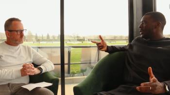 A man interviewing another man, both are seated.