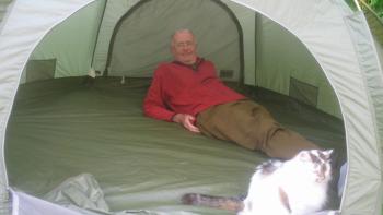 A man lying inside a tent, with a cat in front of him