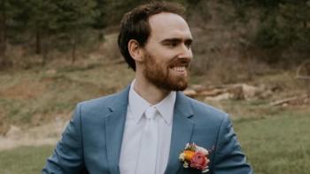 A man in a wedding suit looking to the right and smiling