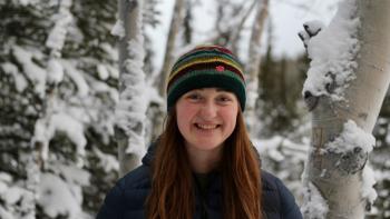A young woman smiling against a snowy forest scene