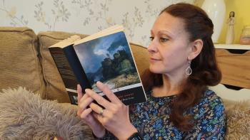 A woman on a sofa reading a paperbook book, with another hardback book on her lap
