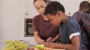 A boy cutting up a lime on a chopping board with his mother looking on. In the background is the father