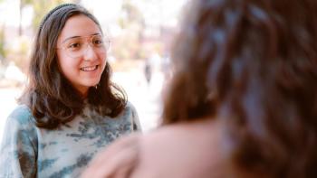 A young woman in conversation with somebody who has their back to us.