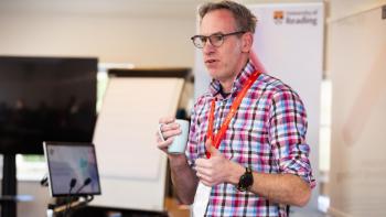 A man wearing a lanyard standing and doing a presentation