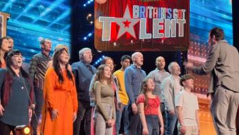 Members of a choir of mixed ages singing on a stage in front of a conductor. Above them is a logo saying 'Britain's Got Talent'