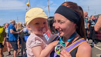 A mother in running gear cuddling her baby daughter and holding up a medal