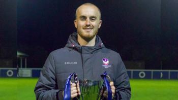 A man standing on a football pitch, holding a trophy and smiling