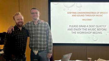 Two men standing beside a projection screen, with their arms around each other