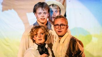 Four actors huddled together on a stage and looking at the camera, in character