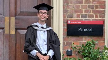 A young man in graduation robes, standing in front of a university door