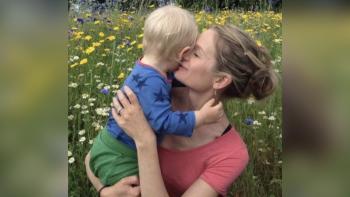 A mother holding her young son in a meadow surrounded by flowers