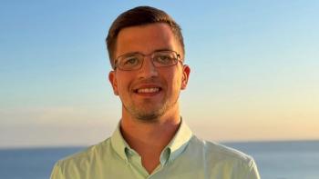 A young man smiling, with the ocean behind him