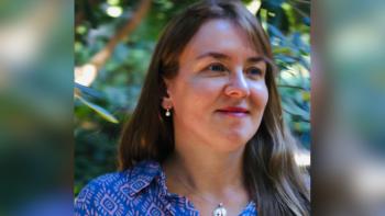 A woman smiling and looking to the right, in front of a tree