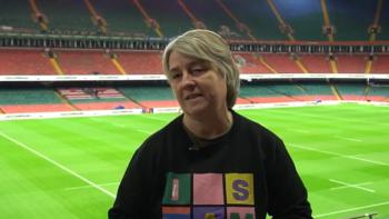 A woman standing in the seated area in a sporting stadium, with the pitch behind her