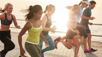 A group of runners, male and female, running next to the coast, with the sun shining behind them
