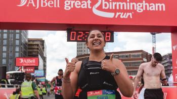 A woman posing at the end of a sponsored run, smiling with her thumbs up