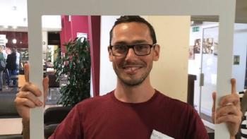 A man looking through a cardboard frame and smiling