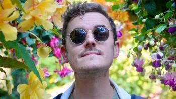 A man wearing sunglasses, standing amid brightly coloured flowers 