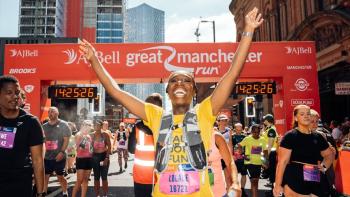 A woman celebrating at the finish line of a sponsored running event, with her hand in the air