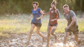 Two women and a man running through mud