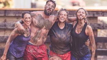 Three women and a man covered in mud posing together at the end of race