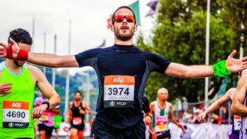 A man in sunglasses crossing the finish line at a sponsored run, with arms outstretched
