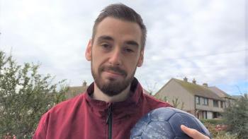 A man in a tracksuit holding a football and smiling
