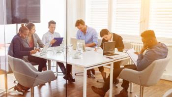 A group of people sitting round a table in a work setting, each one looking at laptops or tablets