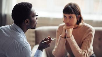 A man talking, with a woman listening to him, looking at him intently with her head resting on both hands