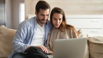 A man and a woman sitting on a sofa looking at a laptop computer